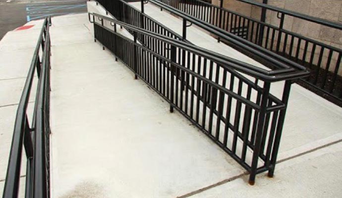 Concrete wheelchair-accessible ramp with black metal railings