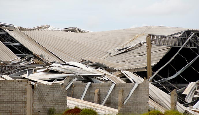 Industrial facility severely damaged with a collapsed metal roof and broken concrete walls after a disaster