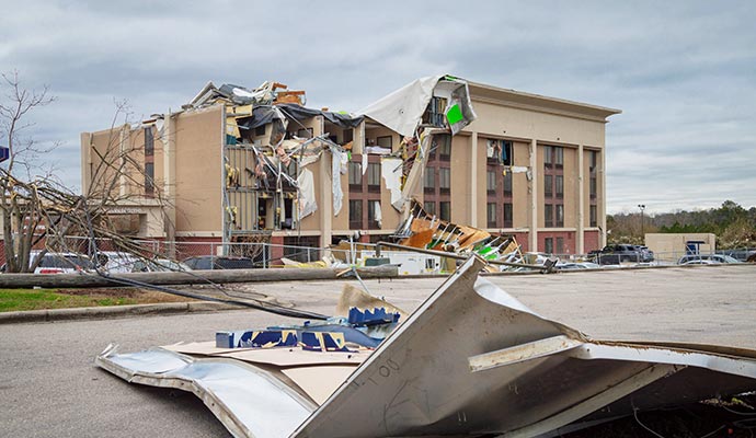 Building exterior severely damaged by strong winds with debris scattered on the ground