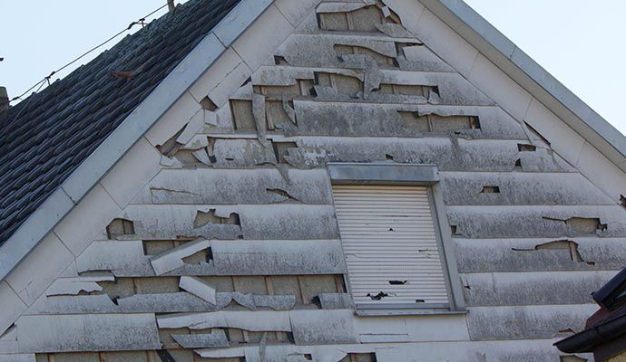 Exterior siding of a house showing severe damage and peeling caused by hail